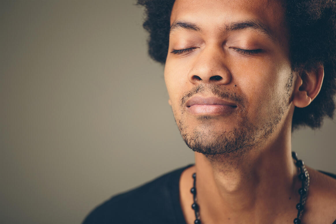 A man closing his eyes breathing in during a meditative state. 